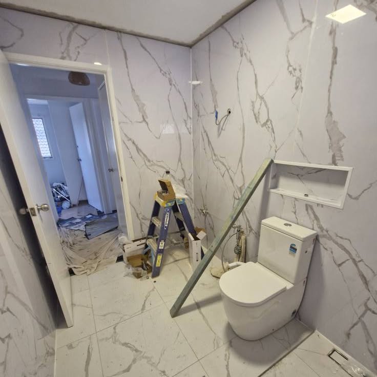 Bathroom mid-renovation with tiles up, toilet installed and a ladder in the room